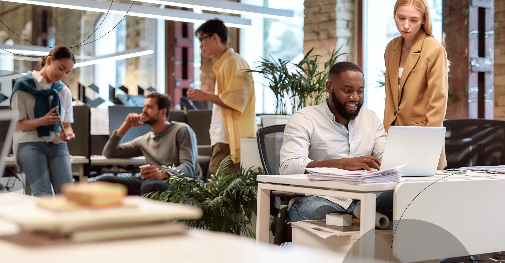 photo of an office with people talking, on the side, a woman standing next to a man smiling at his notebook