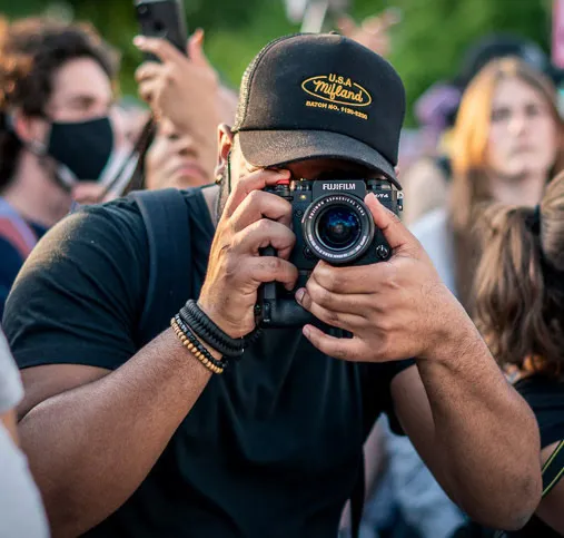 Photo of John Simpson holding a camera facing the viewer